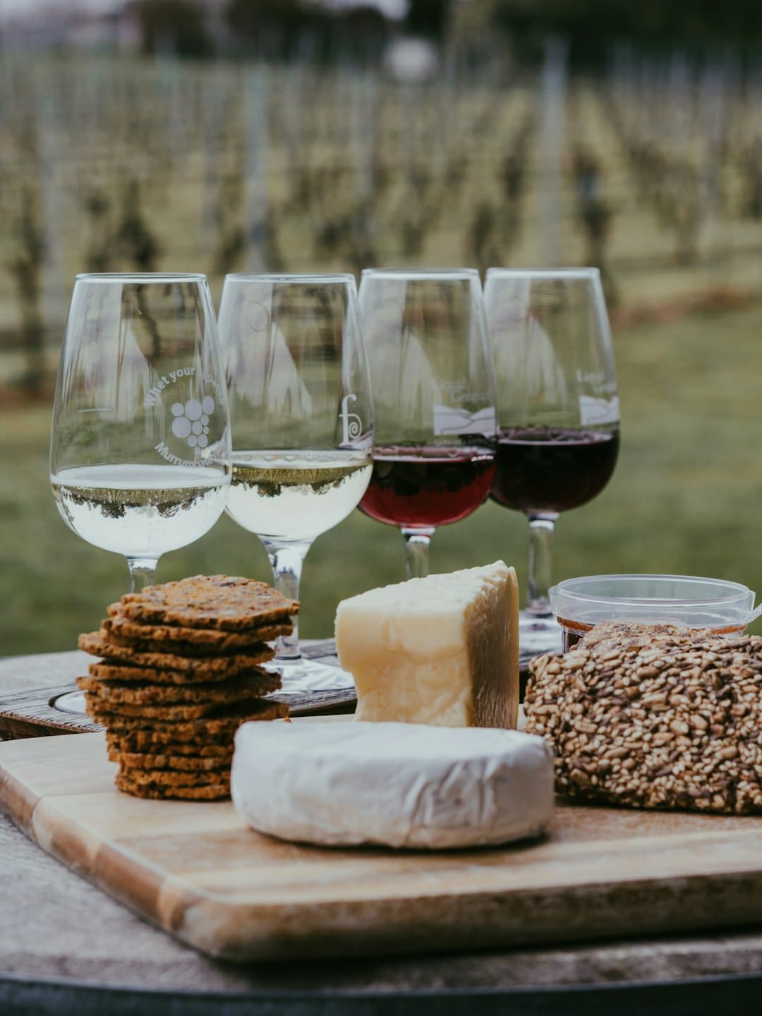 Allestimento per degustazione di vini con formaggio, cracker e vino su un tagliere di legno.