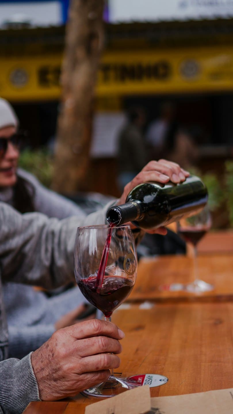Una persona versa vino rosso in un bicchiere su un tavolo all'aperto.